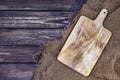 Old chopping board on dark wood background, cutting tray over burlap tablecloth, top view Royalty Free Stock Photo