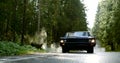 Old classic car is moving on countryside road in forest in daytime, frontal view from ground Royalty Free Stock Photo