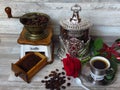 An old classic coffee grinder, silver coffee jar, a cup of coffee and a red rose. Retro style.