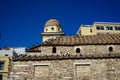 Old classic little church in earth tone natural stone with pigeons on terracotta roof tile with clear blue sky and modern building Royalty Free Stock Photo