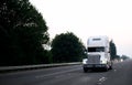 Old classic white high cab big rig power semi truck tractor driving by wide evening highway