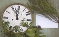 Old clock and blank sheet on the green wood background. New year background with plants and purple berries. Fresh leaves and purpl