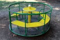 Old colorful outdoor public playground equipment made of metal and wood in shape of roundabout surrounded with gravel and grass in