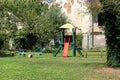 Old colorful outdoor public playground equipment in shape of seesaw and small house with climbing stairs and slide Royalty Free Stock Photo