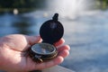 Old compass in the hand of a tourist in front of the reservoir.