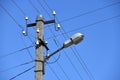 Old concrete electric pole for transmission of wired electricity with lamp post on a background of a cloudy blue sky. Obsolete me Royalty Free Stock Photo