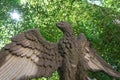 Old concrete garden statue of an eagle with wings spread, green trees behind