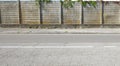 Old concrete precast compound wall with moss and ivy on top. Sidewalk and road in front Royalty Free Stock Photo