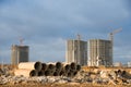 Old concrete sewer pipes for recycling. Salvaging building demolition waste and construction material. Tower cranes working at Royalty Free Stock Photo