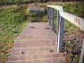 Old concrete stairs with rusty metal railing going down to the green meadow grass in warm bright summer sunlight Royalty Free Stock Photo