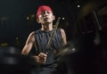 Old cool and talented Asian American mixed ethnicity young boy playing drums in headband practicing and performing song in dark Royalty Free Stock Photo