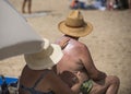 Old couple relax on sand beach. Woman put sunscreen cream on man skin. Wife and husband in hats on sunny day. Love and Royalty Free Stock Photo