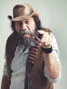 Old cowboy, point and angry face at studio, costume and pipe for western portrait looking scruffy. Senior guy, upset hat