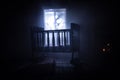 Old creepy eerie baby crib near window in dark room. Scary baby silhouette in dark. A realistic dollhouse living room with Royalty Free Stock Photo