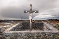 Old cross with crucifix with stone fence near the road