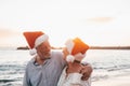 Old cute couple of mature persons enjoying and having fun together at the beach wearing christmas hats on holiday days. Hugged on Royalty Free Stock Photo