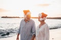 Old cute couple of mature persons enjoying and having fun together at the beach wearing christmas hats on holiday days. Walking on Royalty Free Stock Photo