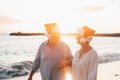 Old cute couple of mature persons enjoying and having fun together at the beach wearing christmas hats on holiday days. Walking on Royalty Free Stock Photo