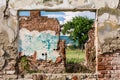 Damaged wall and window frame with view to ruins room and green field of grass Royalty Free Stock Photo