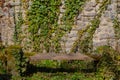 Old damaged and weathered bench in front of a natural stone wall covered with ivy in a graveyard Royalty Free Stock Photo