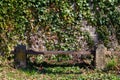 Old damaged and weathered bench in front of a natural stone wall covered with ivy in a graveyard Royalty Free Stock Photo