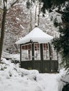 Old dark green gazebo covered with snow. Little wooden garden shelter, cabin in outdoor, park. Beautiful winter garden