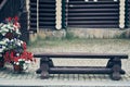 An old dark and low wooden bench against the background of a wooden house. There are garden pots with petunias near the Royalty Free Stock Photo