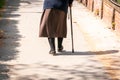 Old depressed woman walk alone down the street with walking stick or cane feeling lonely and lost view from back