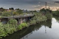 An old, derelict, building, beside a calm canal, overgrown with foliage, set in a urban wasteland
