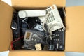 Old desk phones, cordless phone, cell phones and smartphones in a cardboard box