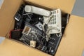 Old desk phones, cordless phone, cell phones, and smartphones in a cardboard box