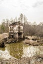 Old destroyed building of the hydroelectric plant with moss-grown walls is located in a forest surrounded by dry grass and shrubs Royalty Free Stock Photo