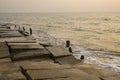 Old destroyed concrete embankment with wooden pillars protruding from the water against the background of ocean waves in the Royalty Free Stock Photo