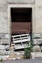 Old dilapidated entrance doors partially covered with rusted metal blinds locked with rusted padlock on top of stacked wooden