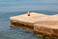 Old dilapidated stone and concrete local pier with strong rusted metal pipe used to tie boats surrounded with calm clear blue sea