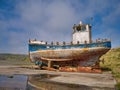 An old, dilapidated wooden fishing boat on blocks in a car park in Cumlewick, Sandwick, Shetland, UK. T