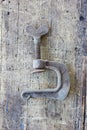 Old, dirty adjustable clamp against wooden plank. Royalty Free Stock Photo