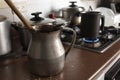 Old dirty cocoa cooking pot over kitchen furniture with gas stove on and others cooking pots at background. Royalty Free Stock Photo