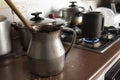 Old dirty cocoa cooking pot over kitchen furniture with gas stove on and others cooking pots at background. Royalty Free Stock Photo