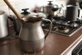 Old dirty cocoa cooking pot over kitchen furniture with gas stove on and others cooking pots at background. Royalty Free Stock Photo