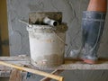 Old dirty grungy bucket and PVC plastic trowel on a wooden stand, being used for cement plastering by a construction worker