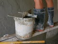 Old dirty grungy bucket and PVC plastic trowel on a wooden stand, being used for cement plastering by a construction worker