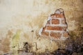 Old dirty and grungy plastered wall facade of an abandoned house with a hole showing the underlying red bricks