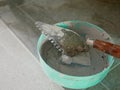 Old dirty grungy trowel in a plastic bowl with tile grunt - tools for grunting the ceramic tile floor - tiling work