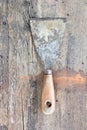 Old, dirty putty knife against wooden plank.