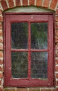 Old dirty window of a brick wall house or home. Ancient casement with red metal frame on a historic building with a