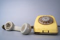 Old dirty yellow rotary telephone with gray removed phone receiver on gray studio background. Antique broken landline Royalty Free Stock Photo