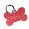 Old dog name tag in shape of bone, red, with name Stella. Memento to remember deceased pet, isolated on white Royalty Free Stock Photo