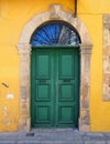 Old double green door in a stone frame in a yellow painted wall typical of the style of old buildings in cyprus