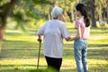 Old elderly using a walking stick to help her walk balanced with her asian granddaughter in outdoor nature,happy senior